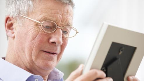 Ein älterer Mann mit Brille betrachtet ein Foto in einem Bilderrahmen.